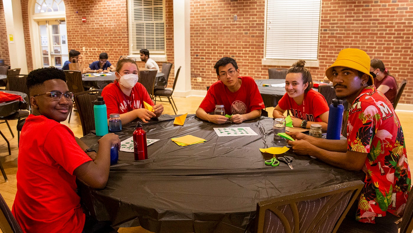 five students sitting at round table doing arts and crafts