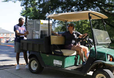 student loading small refrigerator into golf cart driven by DRL staff member