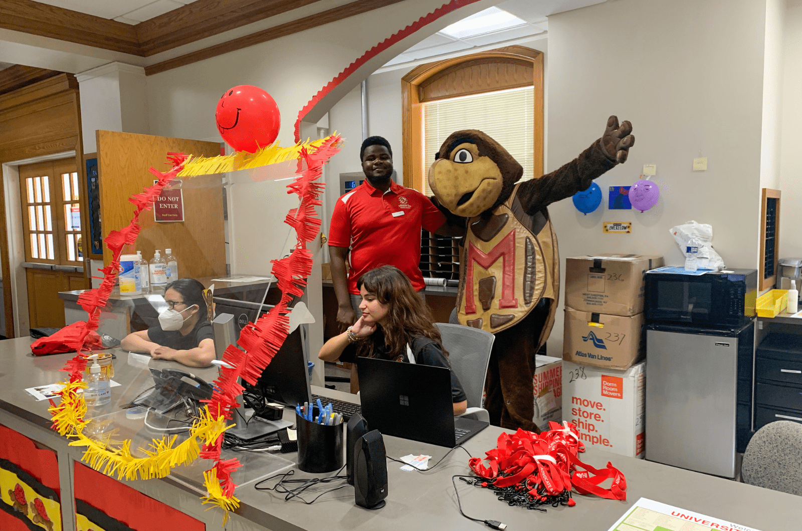 testudo mascot posing with student staff behind service desk